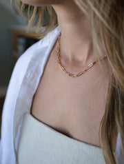 Gold paperclip necklace on the neckline of a model 