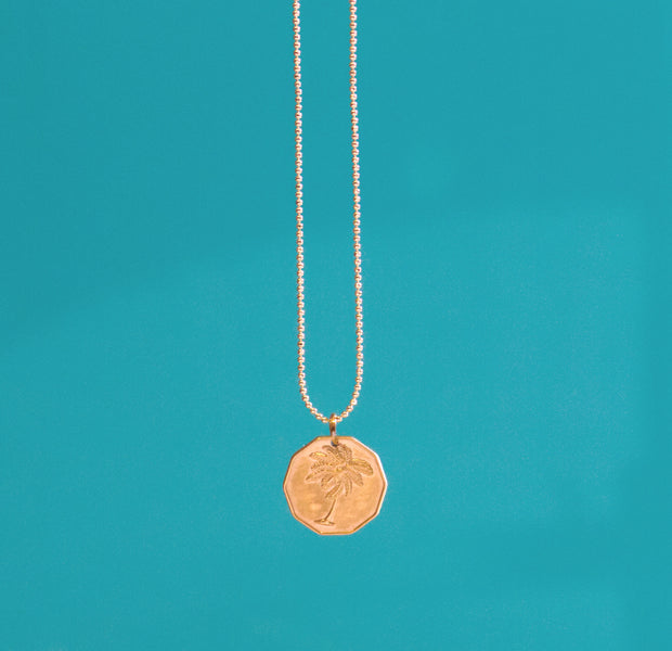 Gold beaded chain necklace with a gold hexagon shaped medallion imprinted with a palm tree.
