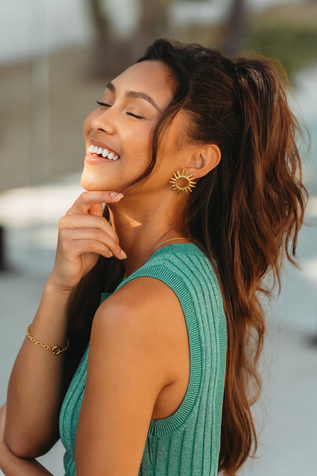 girl wearing green dress and a gold link bracelet with large sun earrings