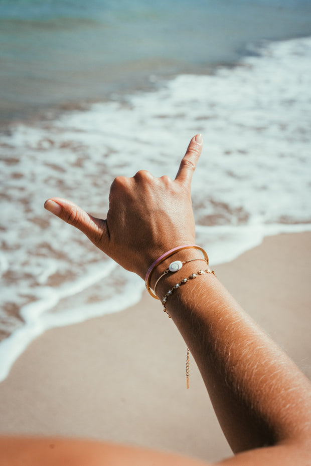 Models hand on the beach wearing a Flat lay of a gold plated bracelet made of small dainty gold flowers connected to make one bracelet.