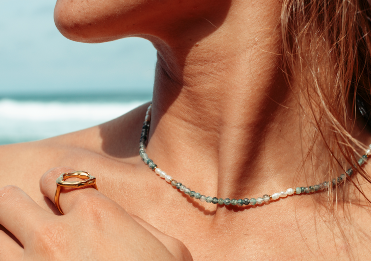 girls neck and hand wearing a gold circle ring and beaded necklace