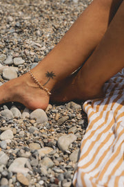 girls foot on rocky beach wearing a gold chain pearl beaded bracelet