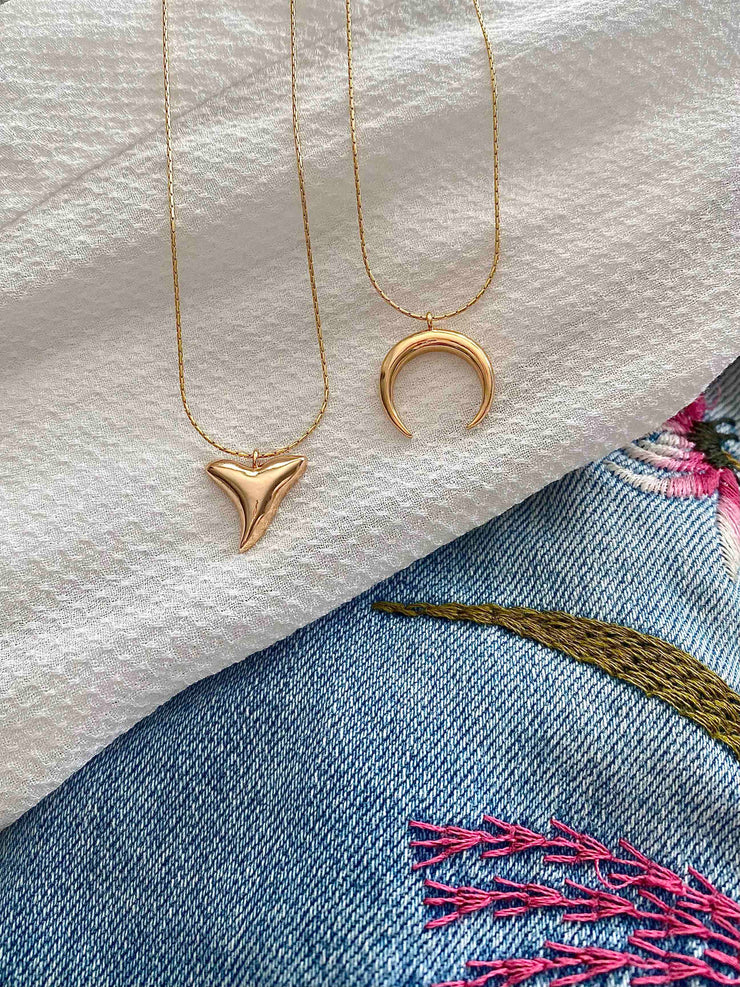 Gold necklace chain with a gold shark tooth pendant next to a gold horn pendant necklace