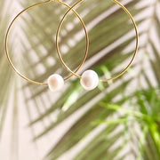 Dainty gold hoop earrings with one white pearl detail on each hoop.