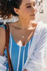 Model in beachy attire wearing a beaded white pearl choker paired with a longer dainty gold chain necklace and small white star pendant
